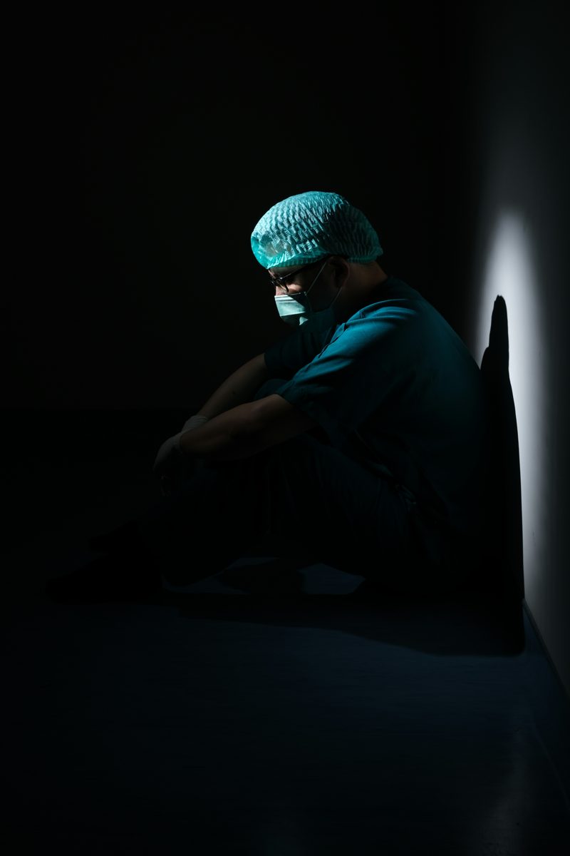 A night-shift clinician sitting in shadow after a long shift